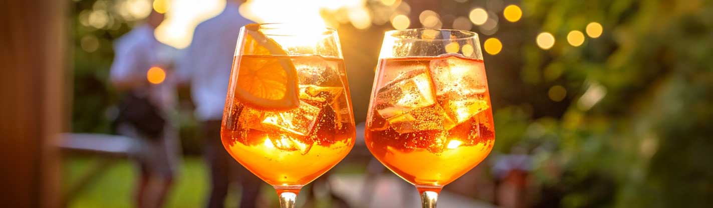Spritz Cocktails bei Sonnenuntergang, unscharfe Gäste bei sommerlichem Afterwork Event